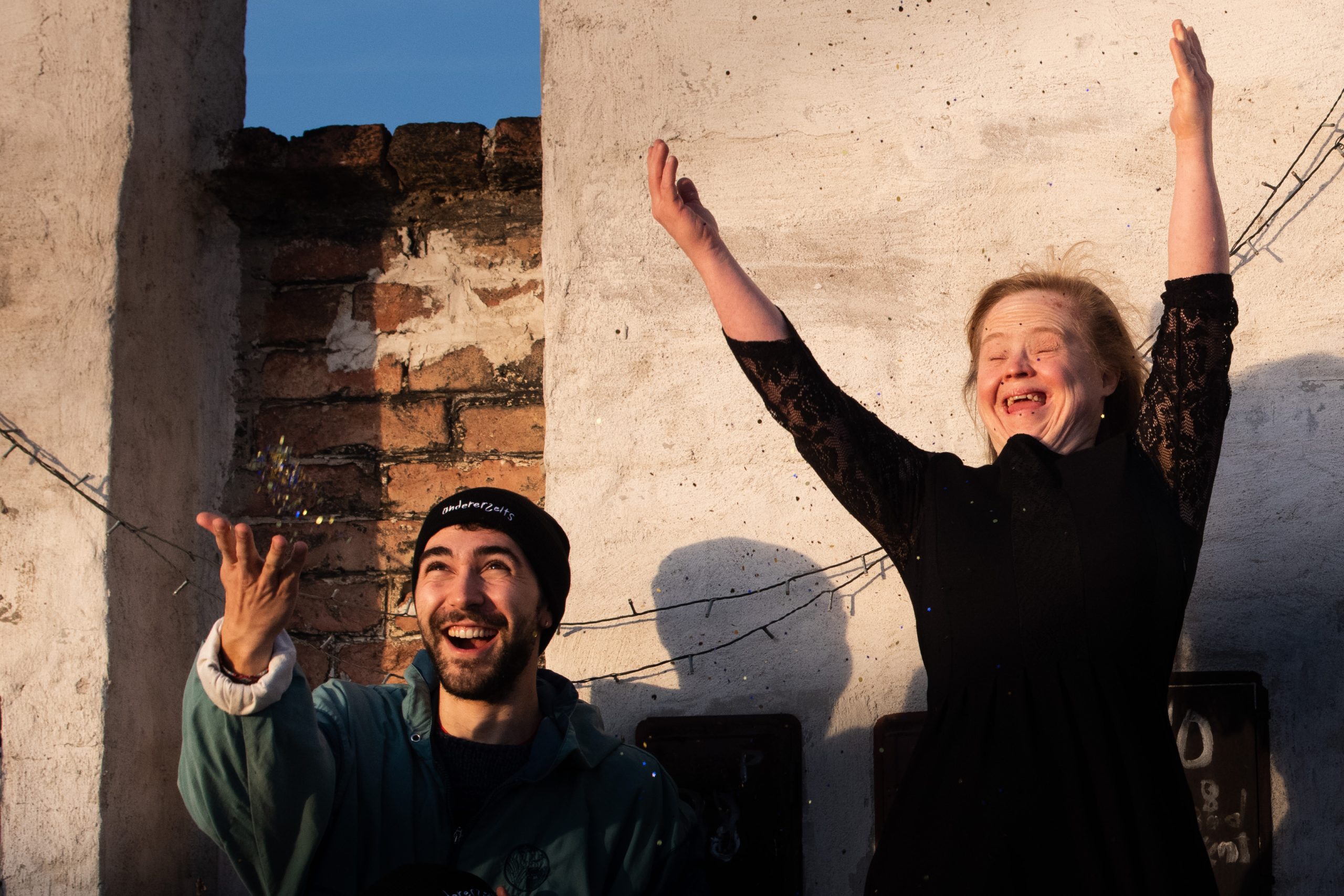 Unterstützer Moritz und Redakteurin Hanna tragen Hauben und werfen Glitzer in die Luft