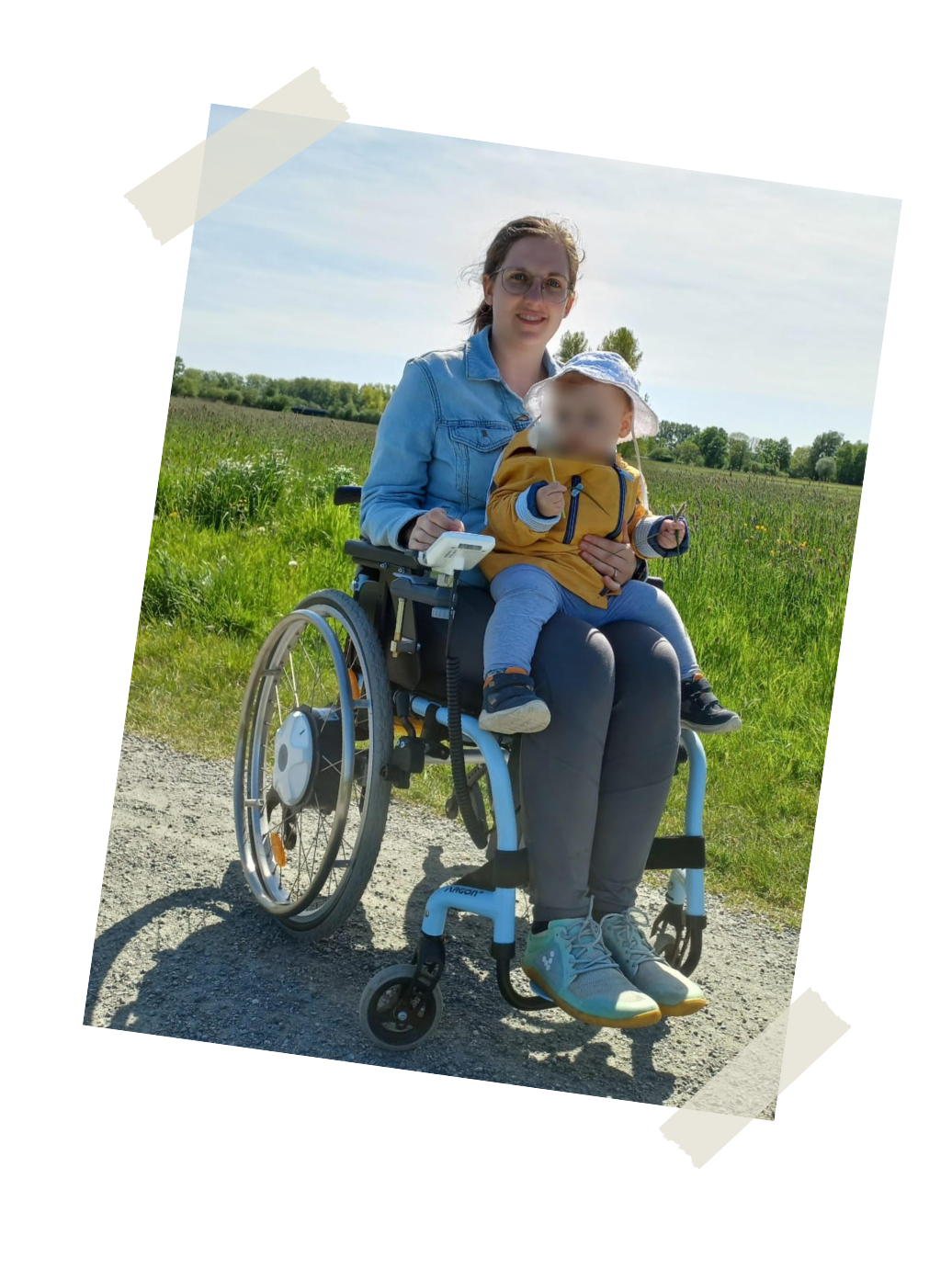 Alina Bindrum sitzt in einem Rollstuhl vor einer grünen Wiese. Auf ihrem Schoß sitzt ihr kleines Kind.