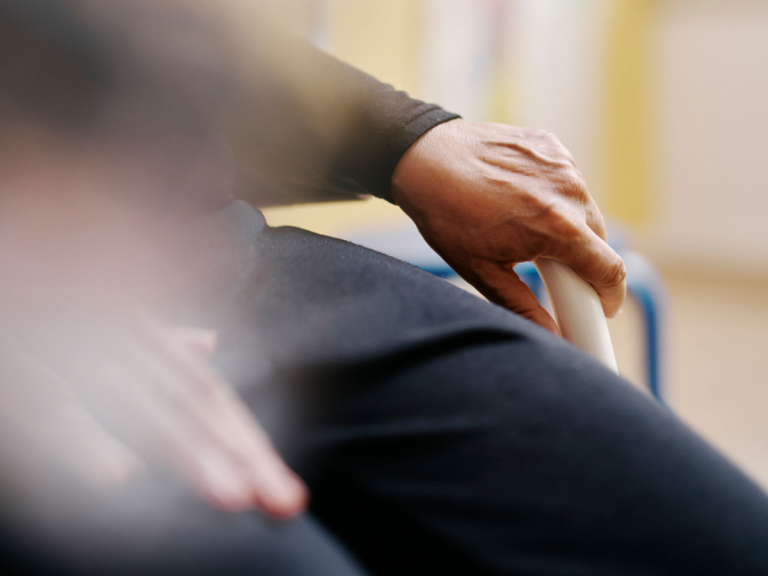 Das Foto zeigt die Hände einer Person, die in einem Stuhl sitzt. Der Hintergrund ist verschwommen.