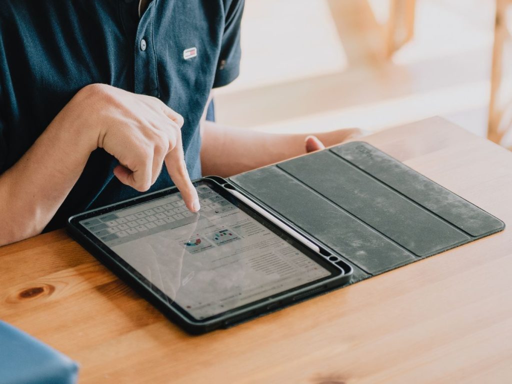 Eine Person bedient mit einer Hand ein Tablet, das auf einem Tisch liegt.