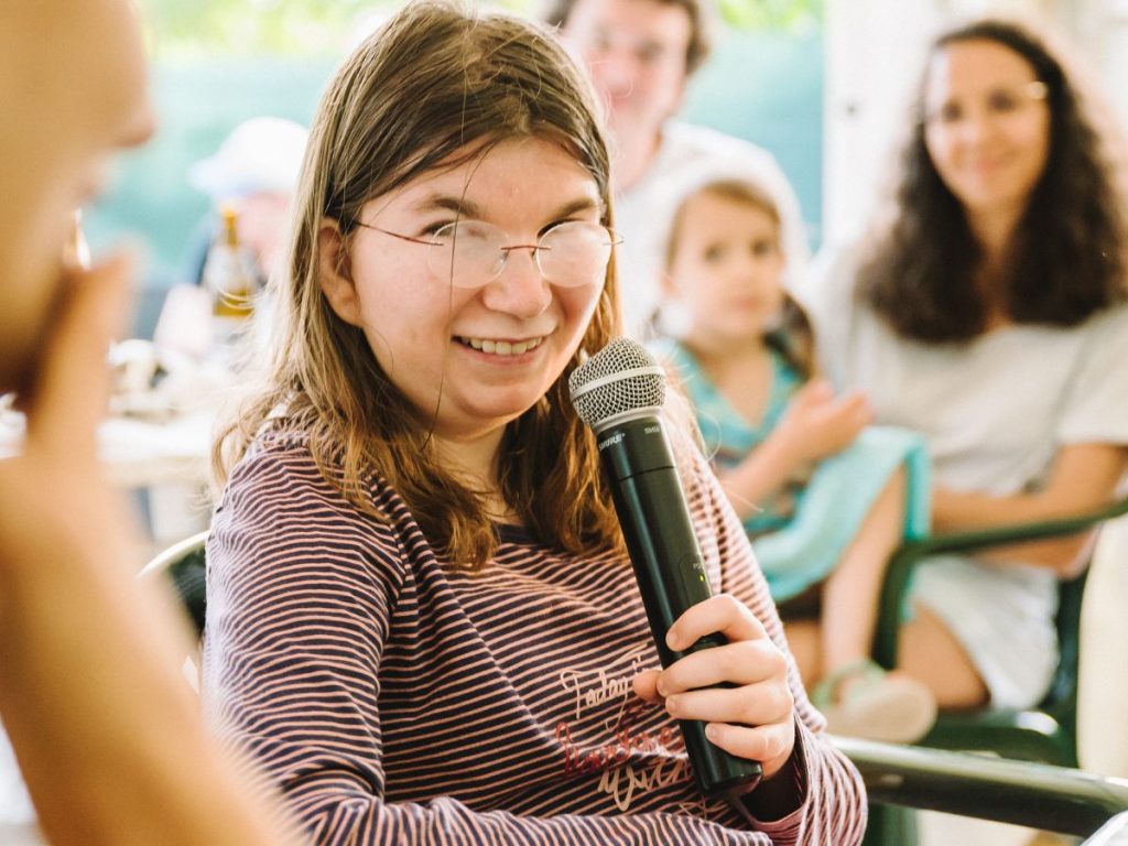 Luise Jäger schaut lächelnd in die Kamera. In der linken Hand hält sie ein Mikrofon.