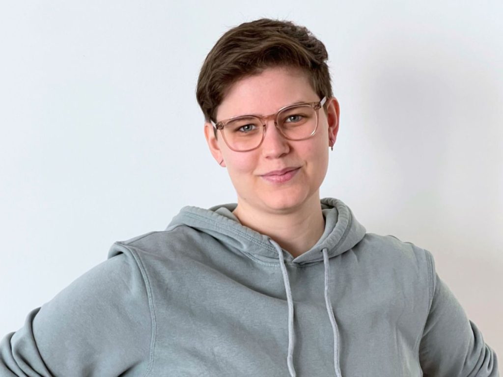 Sven schaut mit freundlichen Blick in die Kamera. Sven trägt eine Brille und kurze, braune Haare.