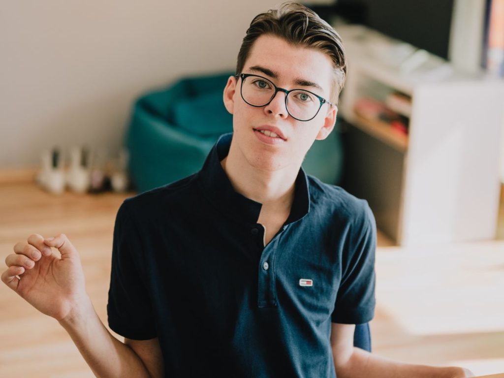 Vincent schaut mit ernstem Blick in die Kamera. Er trägt eine Brille und hat braune Haare.