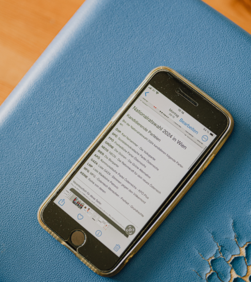 Ein Smartphone liegt auf einem Schreibtisch. Das Display zeigt Informationen zu der Nationalrats-Wahl 2024 an.