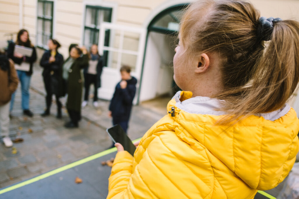 Eine junge Frau in gelber Jacke schaut auf ein Smartphone.