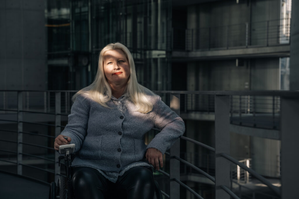 Eine Frau im Rollstuhl blickt in die Kamera. Sie hat lange blonde Haare.