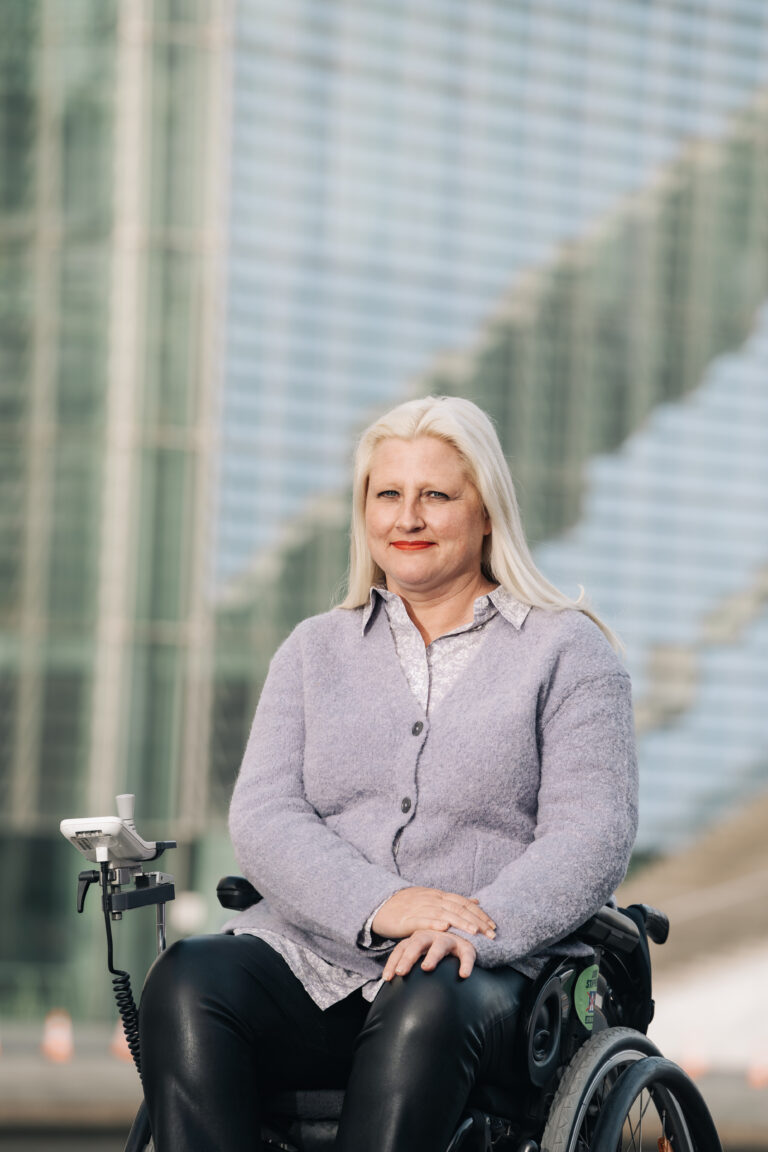 Stephanie Aeffner schaut mit ernstem Blick in die Kamera. Sie ist Politikerin im Bundes-Tag. Sie hat blonde Haare und trägt eine graue Weste. Sie nützt einen Rollstuhl.