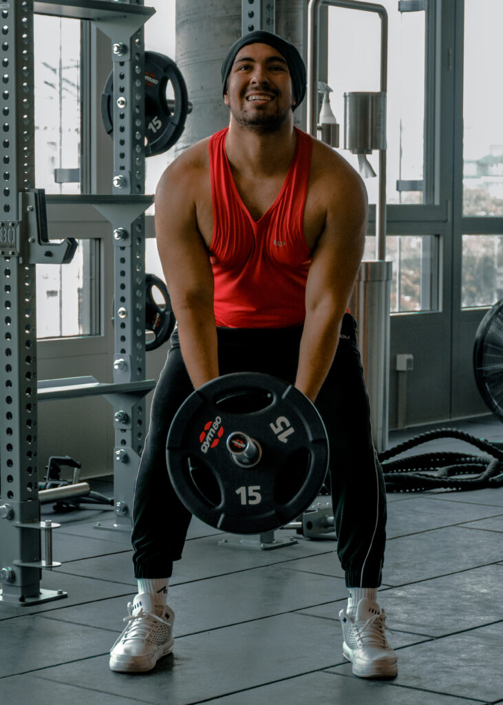 Ein junger Mann hebt in einem Fitnesstudio mit beiden Händen eine Gewichtstange. Er schaut mit angestrengten Blick nach oben.